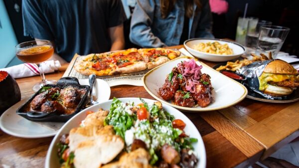 Tablescape dinner table at Von's 1000 Spirits with variety of food including pizza, wings, salad, chicken sandwich, and Mac and cheese