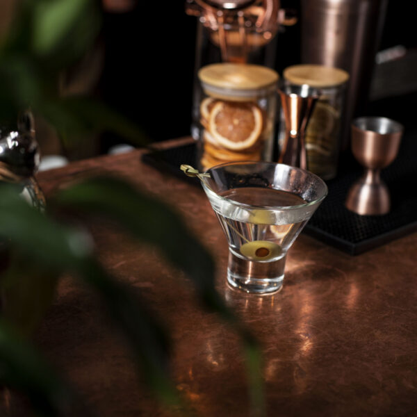 Classic martini with olive garnish served in a cocktail glass on a copper bar.