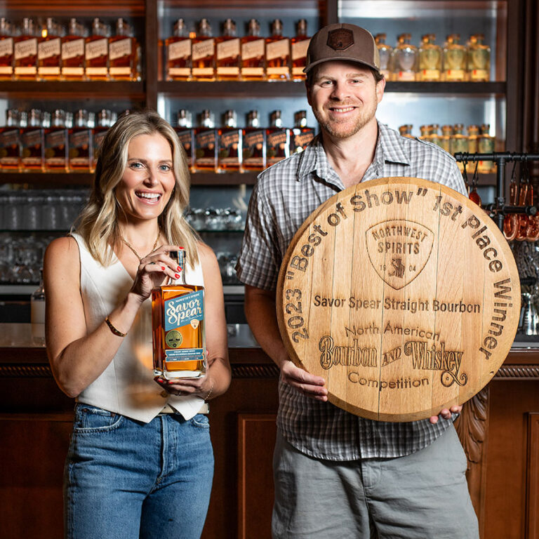 Merissa and Nick smiling and holding a bottle and a large round wooden plaque