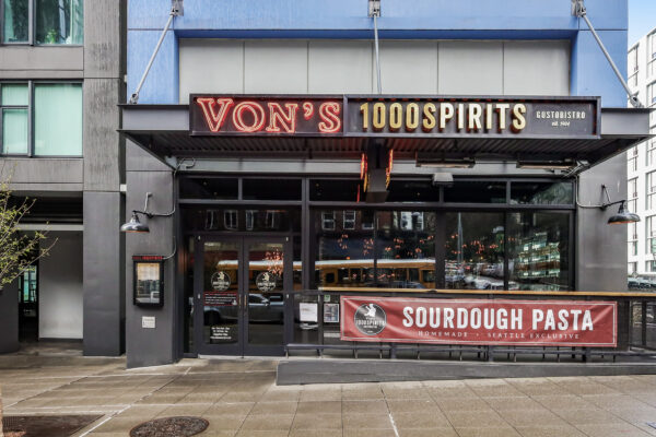 Exterior of Von’s 1000Spirits in downtown Seattle today, featuring the illuminated red “Von’s 1000Spirits” sign above the entrance and a banner highlighting sourdough pasta along First Avenue.