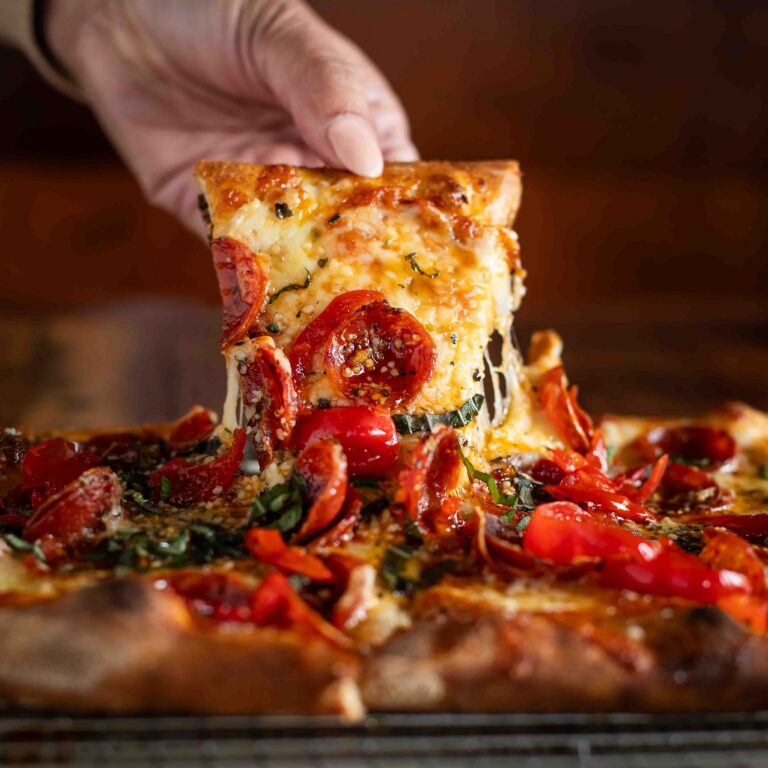 Slice of hot honey pepperoni sourdough pizza being lifted with melted cheese stretch at Von’s