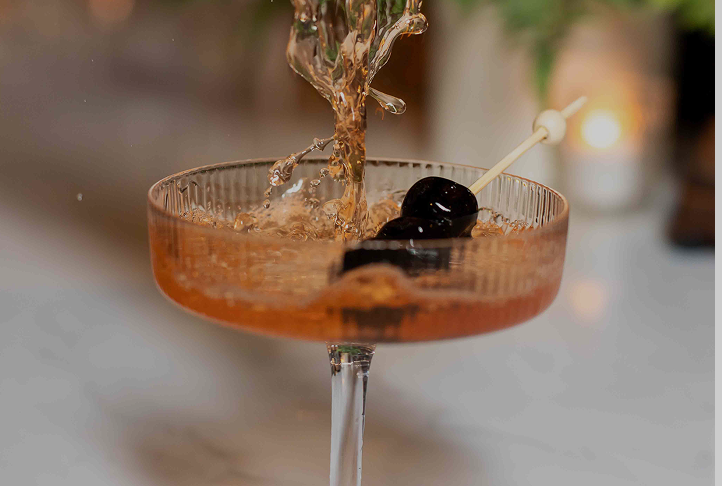 cocktail with two black olives skewered with a toothpick splashing into it