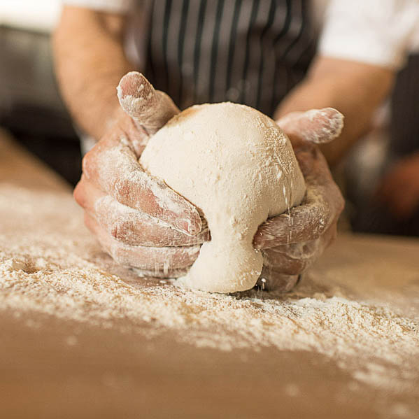 Chef shaping fresh sourdough dough by hand on floured wooden table at Von’s 1000Spirits